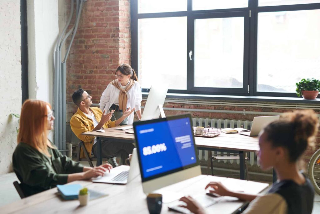 People collaborate in a bright loft office at a long table with laptops and notebooks.