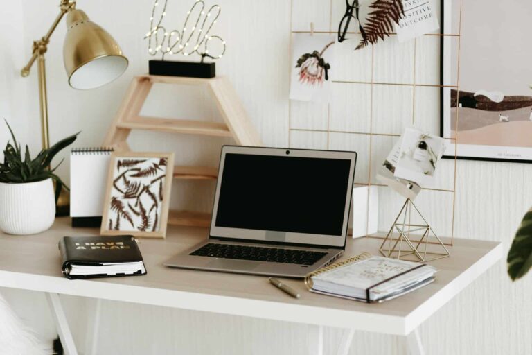 Desk workspace with an open laptop, plant, and decorative items on a white desk.