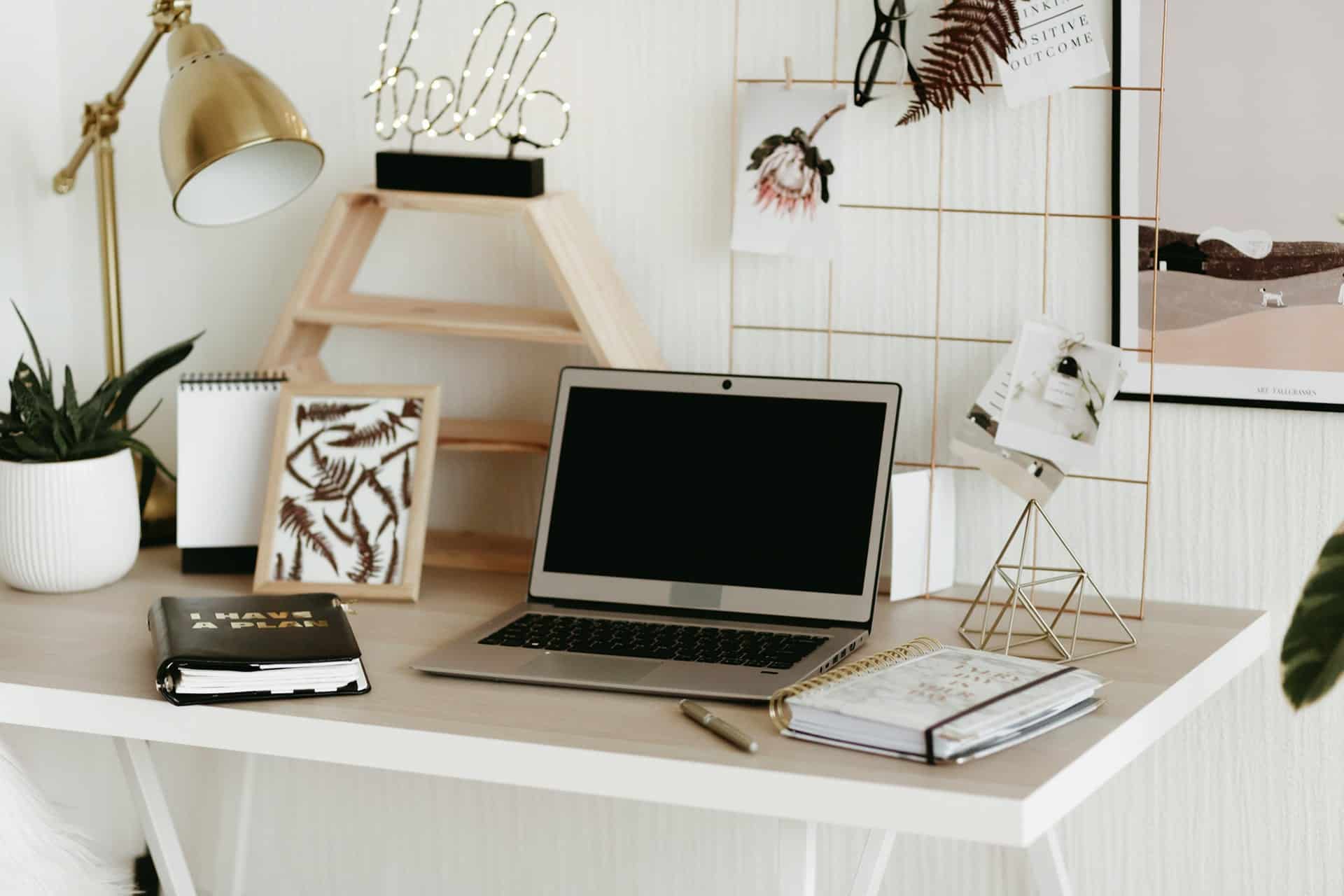Desk workspace with an open laptop, plant, and decorative items on a white desk.