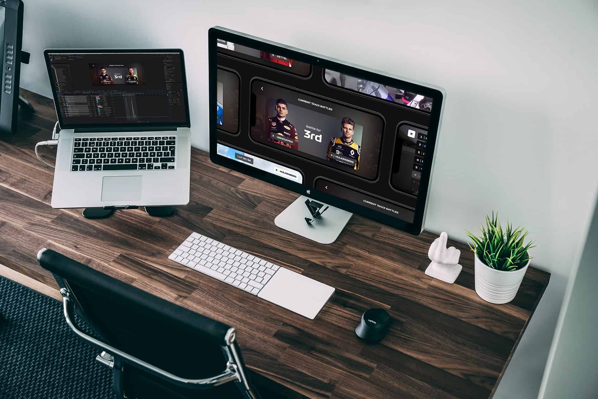 Modern workspace with a laptop and a large monitor showing a game/dashboard on a wooden desk.